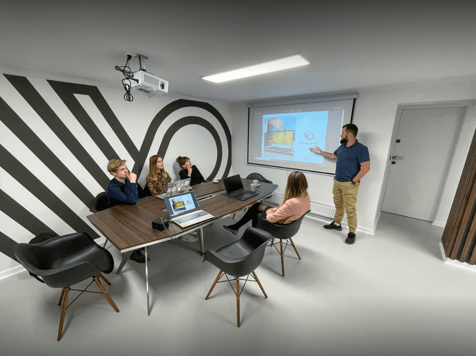 A group of professionals engaged in a presentation in a modern conference room with a striking black and white zigzag wall design