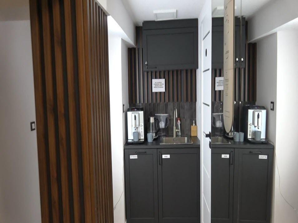 Office kitchenette with modern coffee machines and a clean, minimalist design, featuring wooden accents and instructional signs